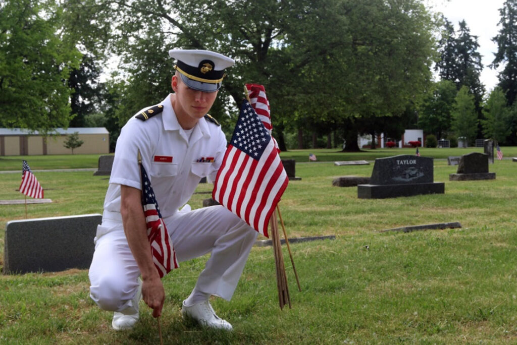 An ROTC cadet from Oregon State University places flags on the graves of military veterans at Crystal Lake Cemetery